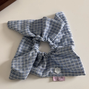 Detailed view of blue checkered hair scrunchie with white flower button and pink tag