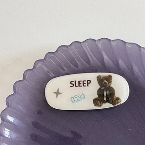 Détail d'une pince à cheveux ovale blanche en résine avec motif ours et texte SLEEP