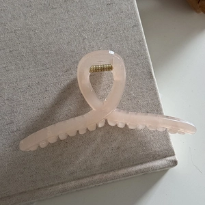 Detailed close-up of translucent pink hair claw clip with golden spring on linen texture