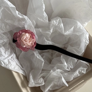 Close-up of pink camellia floral hair pin with black wooden stick on paper background