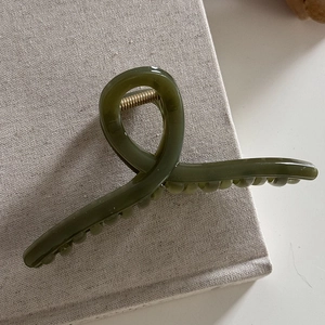 Close-up of minimalist dark green resin hair claw clip with golden metal spring