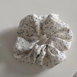 Detail shot of a floral scrunchie with blue flower patterns on cream textured fabric