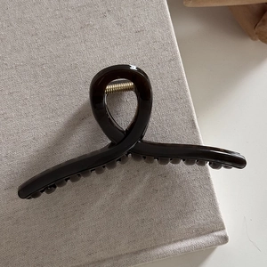 Detail showing high-gloss brown tortoiseshell hair claw clip with metallic spring mechanism