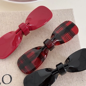 Bow-shaped acetate hair clips set in red, black, and plaid patterns with gold metal grip