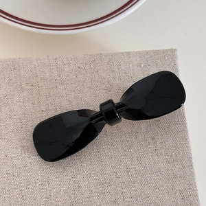 Detail view of a glossy black acetate bow hair clip on a minimalist linen fabric background