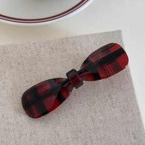 Close-up of red and black tartan plaid acetate hair clip on textured linen fabric