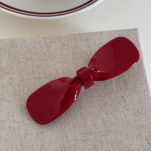Close-up of a glossy red acetate bow hair clip resting on a textured linen fabric background