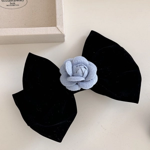 Detailaufnahme einer Samt-Haarspange mit blauer Kamelienblüte auf beigefarbenem Grund