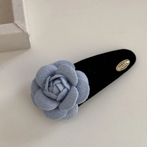 Nahaufnahme einer blauen Samt-Kamelie-Haarklammer mit Goldplakette und Metallbasis