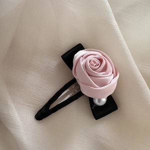 Close-up of pink satin rose hair claw with black ribbon and white pearl detail