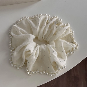 Détails macro d'un chouchou en organza beige avec strass argentés et perles blanches