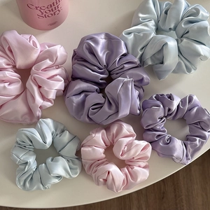 Dettaglio di elastici scrunchies in raso opaco nei colori rosa, viola e blu