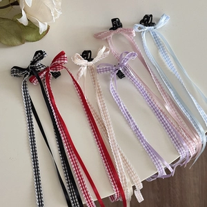 Dettaglio di fermagli per capelli con lunghi nastri a quadri in nero, rosso, beige e colori
