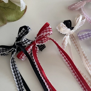 Dettaglio di fermagli per capelli con fiocchi lunghi in nero, rosso e crema a quadri