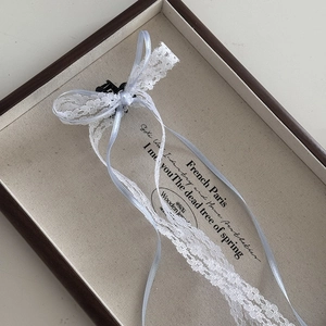Close-up of white lace bow hair clips with ribbons on a vintage display tray