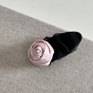 Detail view of pink satin rose hair clip with black mesh netting on a grey linen surface