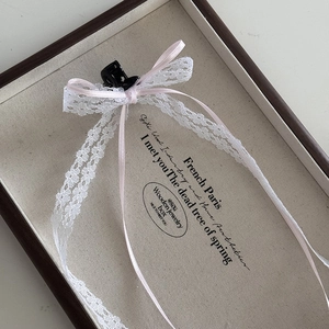 Detailed close-up of a floral lace bow hair claw clip with pink ribbons in a jewelry box