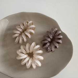 Tre elastici a spirale per capelli nei toni marrone e crema su vassoio in ceramica