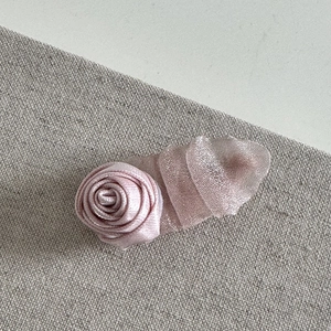 Detail shot of a pink fabric rose hair clip featuring soft satin petals and mesh layers