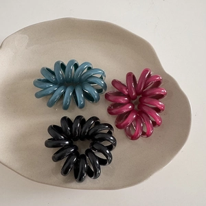 Dettaglio di tre elastici per capelli a spirale colorati su un vassoio di ceramica beige