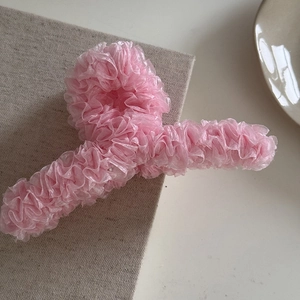 Détail d'une grande pince à cheveux rose avec volants en organza sur fond de tissu texturé