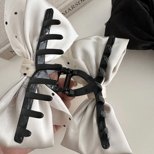 Detail showing high-gloss black claw clip with white polka dot satin bow decoration