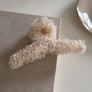 Détail de la grande pince à cheveux en organza beige plissé sur un tissu en lin naturel