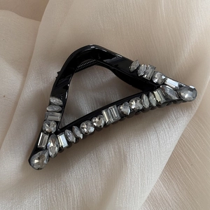 Detail shot of a black triangular hair claw clip with sparkling rhinestones on silk fabric
