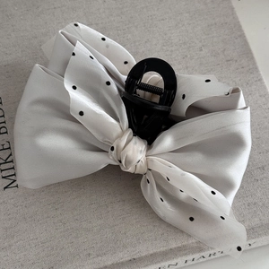 Detailed view of the creamy satin bow hair claw with black polka dots on a book background