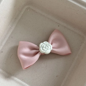 Dettaglio del fermaglio con fiocco in raso rosa e fiore di camelia bianca su vassoio
