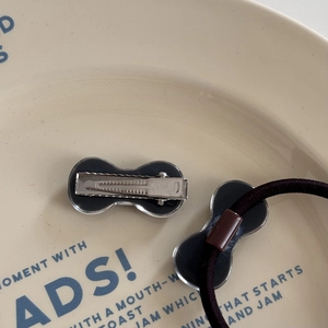 Close-up of black acrylic bow hair clip and elastic hair tie on a decorative ceramic plate