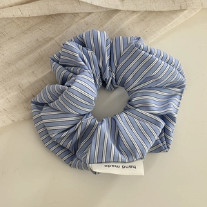 Detailed close-up of blue and white striped fabric scrunchie with handmade woven label