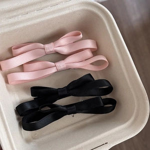 Détail de quatre barrettes à nœuds en satin rose et noir sur support en papier