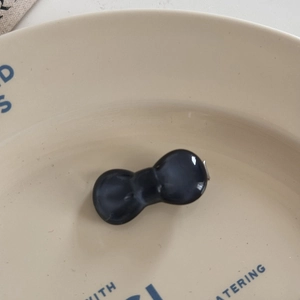 Macro view of glossy black resin bow hair tie placed on a decorative cream ceramic plate