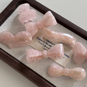Vue macro détaillée de barrettes à cheveux en acétate rose sur un plateau en bois
