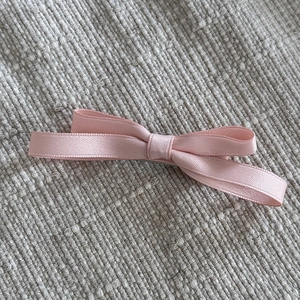 Détail d'une pince à cheveux avec nœud en ruban satin rose sur tissu tressé gris