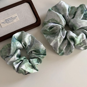 Detail of two satin scrunchies featuring green and white marble tie-dye oil painting pattern
