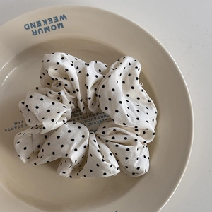 Gros plan d'un chouchou en satin crème à pois noirs sur une assiette en céramique