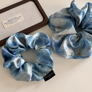 Detail of two blue oil painting satin hair scrunchies with elegant fabric texture