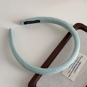 Detail of light blue fabric headband featuring a black handmade label on woven material