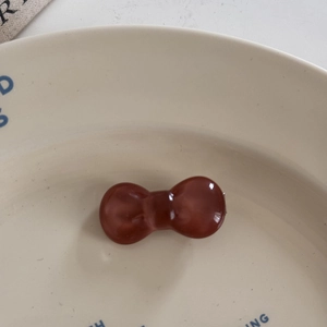 Close-up of translucent amber bow hair tie on a minimalist white ceramic display plate