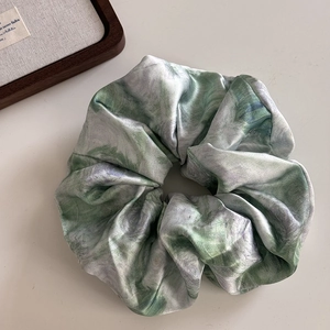 Detailed close-up of green marble pattern satin scrunchie with soft silky luster