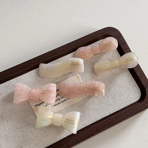 Gros plan détaillé de barrettes à cheveux en acétate rose et blanc sur un plateau bois