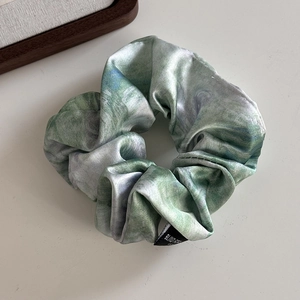 Close-up of elegant satin scrunchie with green and purple oil painting texture
