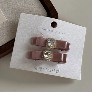 Détail de deux barrettes à nœuds en satin rose avec strass brillants sur une carte