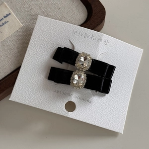 Détail de deux barrettes à nœuds en satin noir avec strass sur carte de bijoux