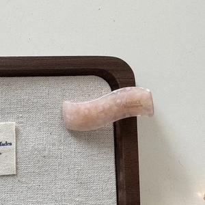 Détail de la pince à cheveux ondulée en acétate rose clair avec texture marbrée