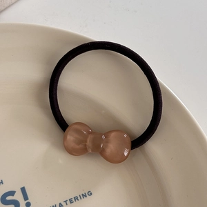 Close-up of a brown resin bow on a black elastic hair tie inside a beige ceramic plate