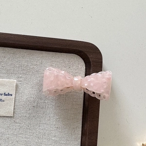 Détail d'une barrette à nœud en acétate rose pâle avec bordure à motifs ondulés