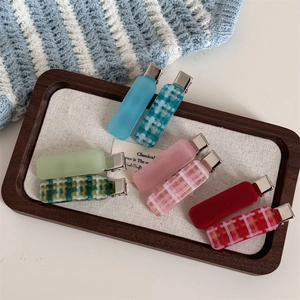 Close-up of matte and plaid acetate hair clips in a wooden tray with a cozy knit background